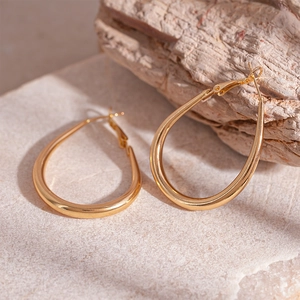 Detailed macro view of golden teardrop hoop earrings on a textured stone surface