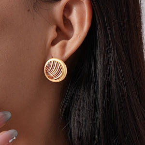 Detailed close-up of golden round geometric earrings with textured wave patterns on model
