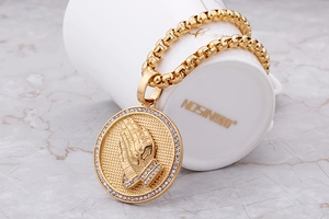 Macro shot of 18K gold plated prayer hands round pendant with sparkling zircon bezel