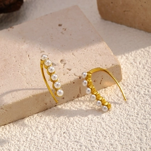 Detailed close-up of gold hoop earrings with six white pearls on stone background
