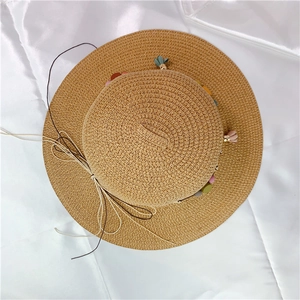 Detail view of straw sun hat featuring colorful pom-poms, tassels and elegant side bow