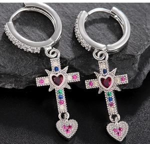 Macro shot of silver heart and cross earrings with multi-color zircons on dark rock
