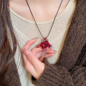 Dettaglio della collana a croce in nastro scozzese rosso con fiori di velluto