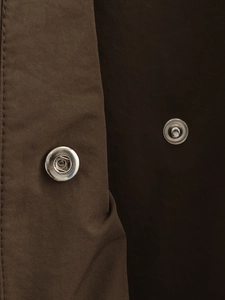 Macro detail of dark brown trench coat fabric featuring two polished metal snap buttons