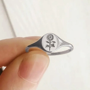 Close-up of a silver signet ring featuring a detailed sunflower engraving on oval face