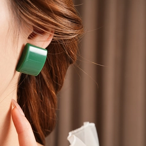 Macro laterale di una modella che indossa orecchini quadrati in resina verde con finitura liscia