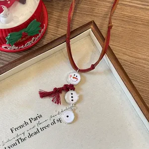 Détail du collier bonhomme de neige avec cordon en cuir rouge et pompon sur tissu