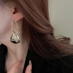 Minimalist gold geometric earrings featuring a cutout triangle pendant on model