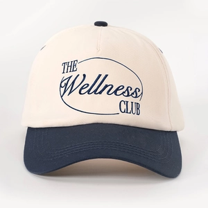 Detail of THE Wellness CLUB embroidery on two-tone cream and navy cotton baseball cap