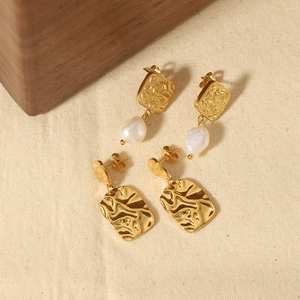 Gold titanium steel square hammered earrings with freshwater pearls on linen surface