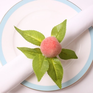 Close-up of artificial peach and green leaf napkin ring on a white ceramic plate