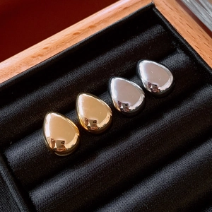 Detail showing gold and silver teardrop earrings on black velvet in a wooden box