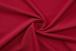 Detail of dark red knitted fabric texture with elegant spiral pleated folds design