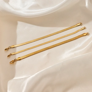 Three gold stainless steel flat snake chain bracelets in various widths on white silk