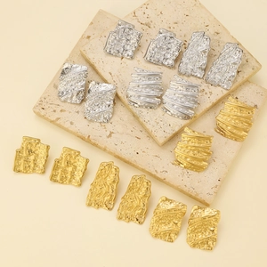 Detailed view of hammered gold and silver irregular square earrings on stone texture