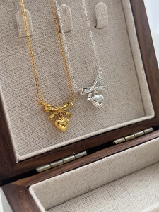 Detail of silver and gold bow heart necklaces displayed in a premium wooden jewelry box