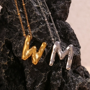 Detail van de gouden letter W en zilveren letter M hangers met lava ontwerp