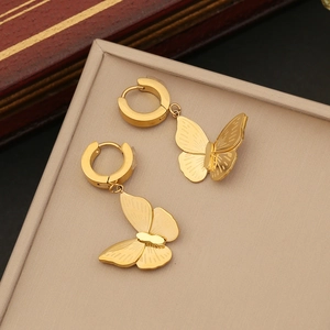 Golden butterfly hoop earrings with textured wings on a beige jewelry display pad
