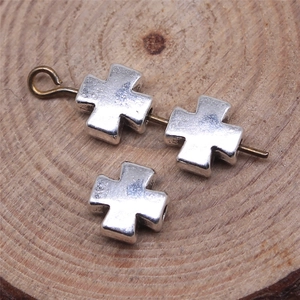 Silver cross beads and needle for DIY jewelry making on a rustic wood slice background