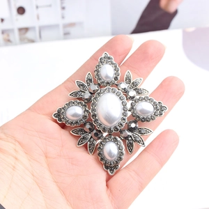Close-up of vintage silver cross brooch featuring white pearls and grey rhinestones