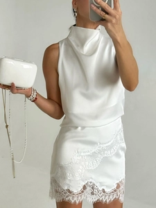 Detail of white satin sleeveless top with high neck and delicate lace trim on the skirt