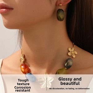Détail du collier de perles en résine colorée avec fleurs dorées et boucles d'oreilles vertes