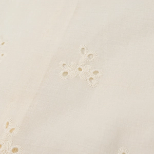Macro shot of off-white fabric with delicate floral eyelet embroidery and cotton texture