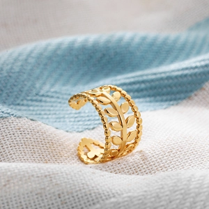Detail shot of a golden open leaf ring featuring an olive branch design on blue fabric