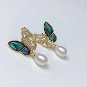 Macro shot of gold butterfly earrings with pearl pendants and sparkling zircon stones
