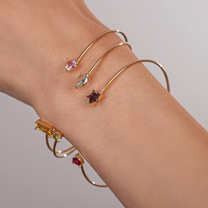 Détail de bracelets dorés superposés avec breloques en zircon coloré et étoiles