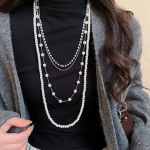 Detail of layered pearl and silver chain necklace worn over a black sweater top