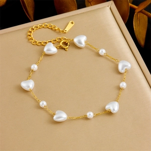 Elegant gold chain bracelet with white heart-shaped pearls on a beige display mat