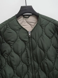 Detail of dark green quilted jacket featuring a metal zipper and onion stitching patterns
