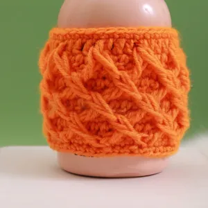 Detailed view of handmade orange crochet cup sleeve with 3D diamond knit pattern