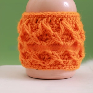 Detailed view of handmade orange crochet cup sleeve with 3D diamond knit pattern