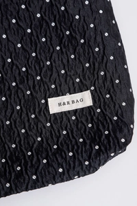 Macro detail of black polka dot fabric with pleated texture and H&R BAG woven label