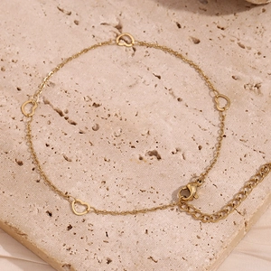 Detail of 14K gold plated anklet with hollow heart charms on textured stone surface