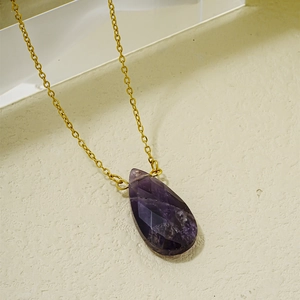 Vue macro d'un pendentif en pierre violette en forme de goutte sur chaîne dorée