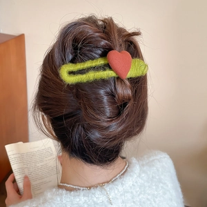 Detail of green knitted hair clip with red heart ornament on a textured bun hairstyle
