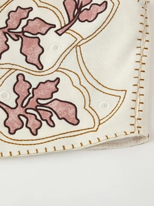 Detail of floral embroidery on beige fabric with brown stitching and leaves
