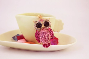 Detail of pink crystal owl keychain with gold metal frame next to heart-shaped saucer