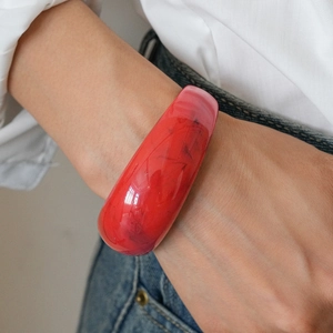 Close-up of vibrant red thick resin open bangle on wrist with natural swirl patterns