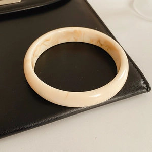 Close-up of ivory resin round bangle with marble pattern on a black leather surface