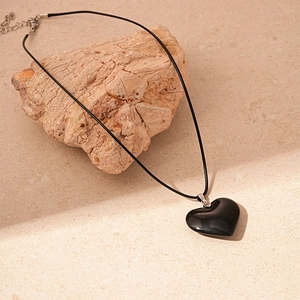Minimalist black heart pendant necklace with leather cord on natural stone backdrop