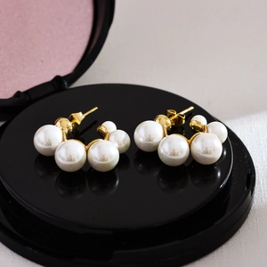Macro detail of elegant gold-tone pearl earrings on a black textured background