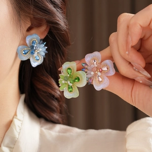 Gros plan de boucles d'oreilles fleur en cristal bleu, vert et rose sur l'oreille