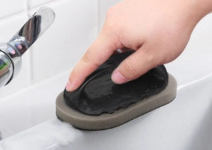 Close-up of a grey emery sponge brush with black handle cleaning a white kitchen sink edge