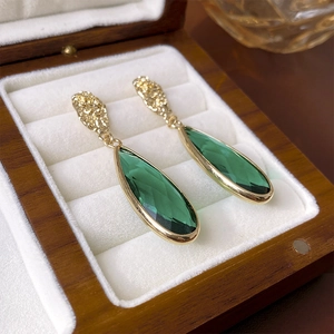 Detail of vintage gold earrings with green faceted teardrop stones in a jewelry box