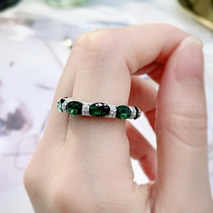 Detail of silver eternity ring with five oval green gemstones worn by a model