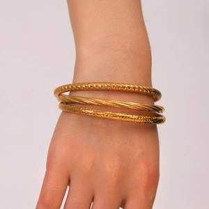 Detail showing three gold-tone textured stainless steel bangles on a woman's wrist